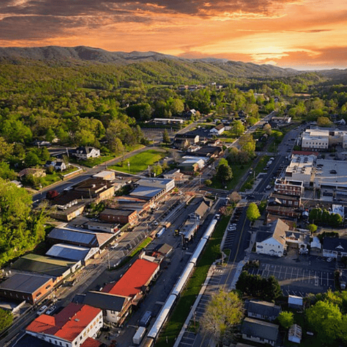 Aerial view of a green mountain town with railway tracks and streets at sunset.