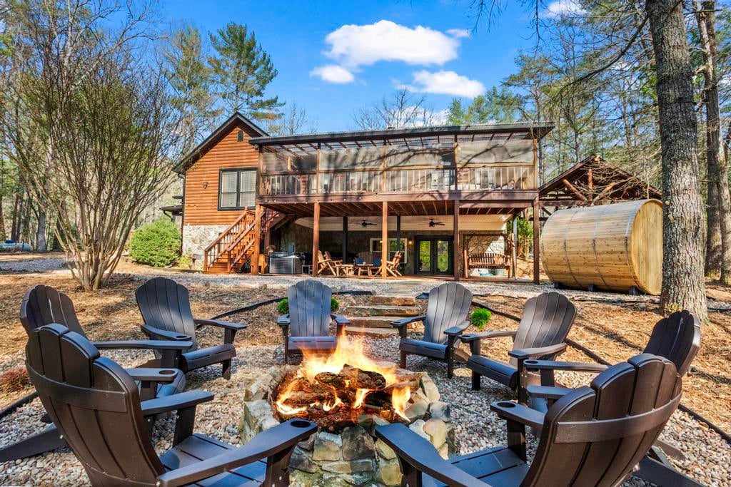 Rustic log cabin with screened porch, barrel sauna, and Adirondack chairs around a blazing fire pit.
