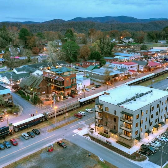 Aerial dusk view of a small autumn-colored town with a freight train, streets, buildings, and mountains.