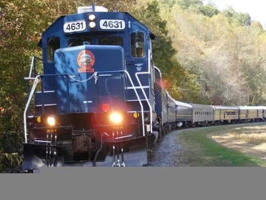 Blue locomotive 4631 pulling silver passenger cars around a wooded curve.
